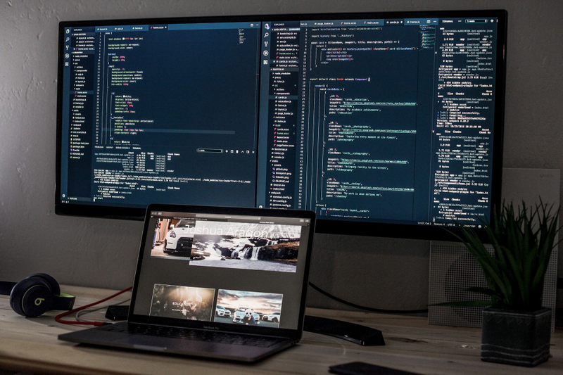 Laptop and large monitor with code on stop of a wooden desk